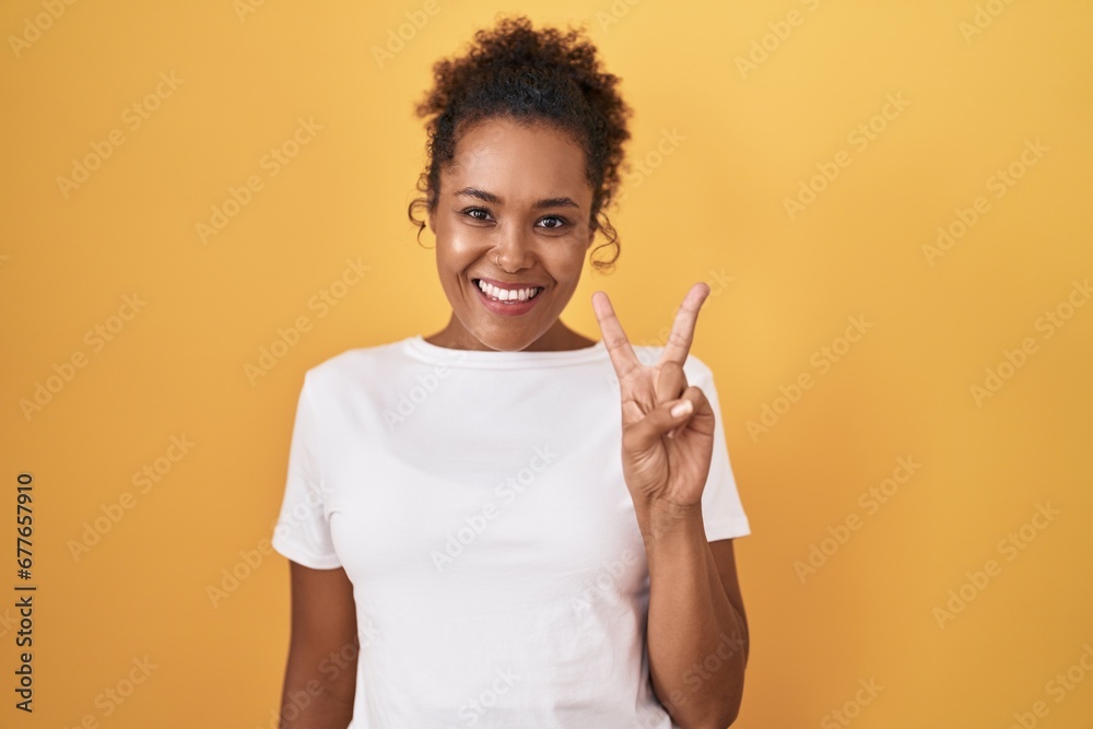 Young hispanic woman with curly hair standing over yellow background showing and pointing up with fingers number two while smiling confident and happy. Young hispanic woman with curly hair standing over yellow background showing and pointing up with fingers number two while smiling confident and happy.