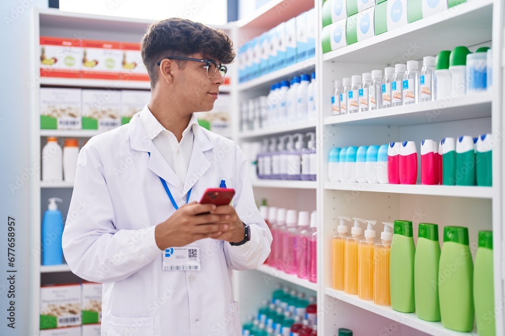 Young hispanic teenager pharmacist using smartphone working at pharmacy