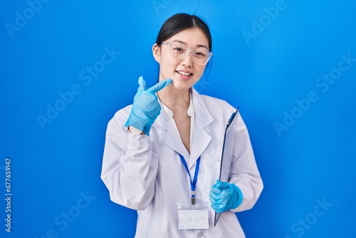 Chinese young woman working at scientist laboratory smiling cheerful showing and pointing with fingers teeth and mouth. dental health concept.