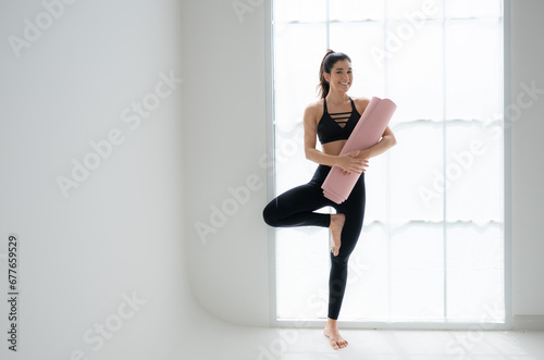 Fototapeta Naklejka Na Ścianę i Meble -  Full length portrait of a young woman holding yoga mat isolated on white background