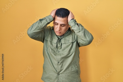 Hispanic young man standing over yellow background suffering from headache desperate and stressed because pain and migraine. hands on head. © Krakenimages.com