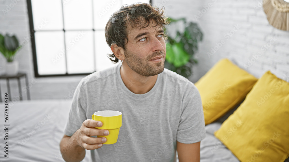 Handsome young blond man relaxing in cozy pj's on bedroom bed, hispanic guy with beard and serious expression awakening indoors, enjoying morning espresso drink in comfortable apartment room. Handsome young blond man relaxing in cozy pj's on bedroom bed, hispanic guy with beard and serious expression awakening indoors, enjoying morning espresso drink in comfortable apartment room.