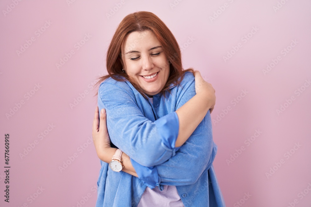Young hispanic woman with red hair standing over pink background hugging oneself happy and positive, smiling confident. self love and self care Young hispanic woman with red hair standing over pink background hugging oneself happy and positive, smiling confident. self love and self care