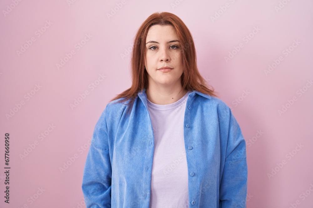 Young hispanic woman with red hair standing over pink background relaxed with serious expression on face. simple and natural looking at the camera. Young hispanic woman with red hair standing over pink background relaxed with serious expression on face. simple and natural looking at the camera.