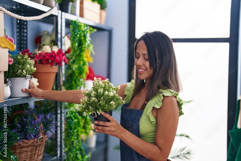 Young hispanic woman florist holding plant pot at florist store