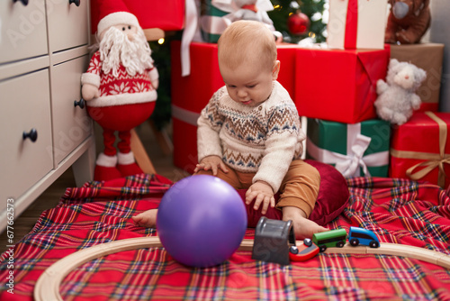 Adorable caucasian baby playing with train toy sitting on floor by christmas gifts at home