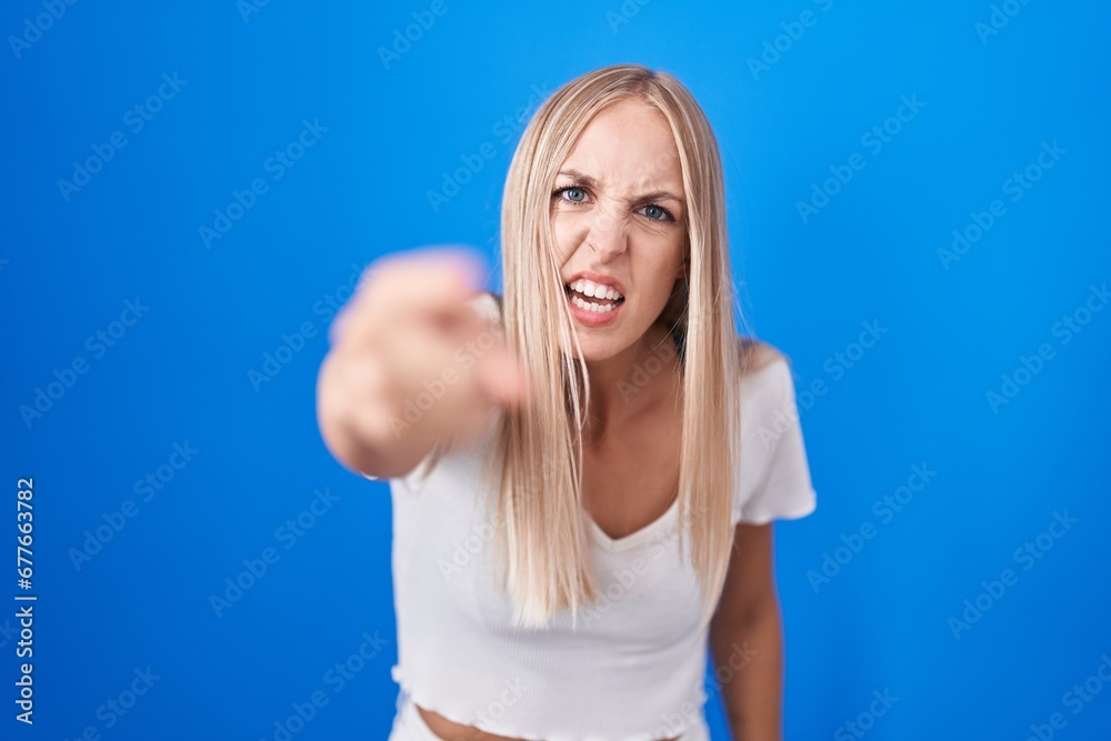 Young caucasian woman standing over blue background pointing displeased and frustrated to the camera, angry and furious with you