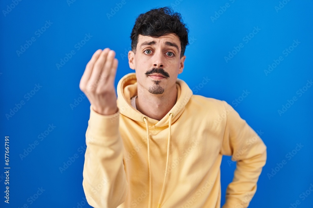Hispanic man standing over blue background doing italian gesture with hand and fingers confident expression Hispanic man standing over blue background doing italian gesture with hand and fingers confident expression