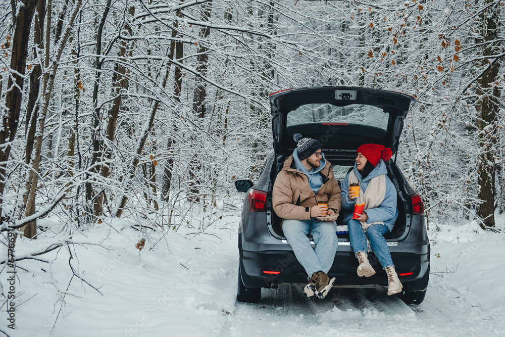 In a snowy winter forest, a couple drinks coffee in their trunk