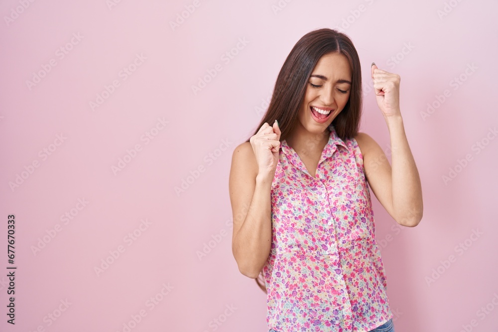 Young hispanic woman with long hair standing over pink background very happy and excited doing winner gesture with arms raised, smiling and screaming for success. celebration concept. Young hispanic woman with long hair standing over pink background very happy and excited doing winner gesture with arms raised, smiling and screaming for success. celebration concept.