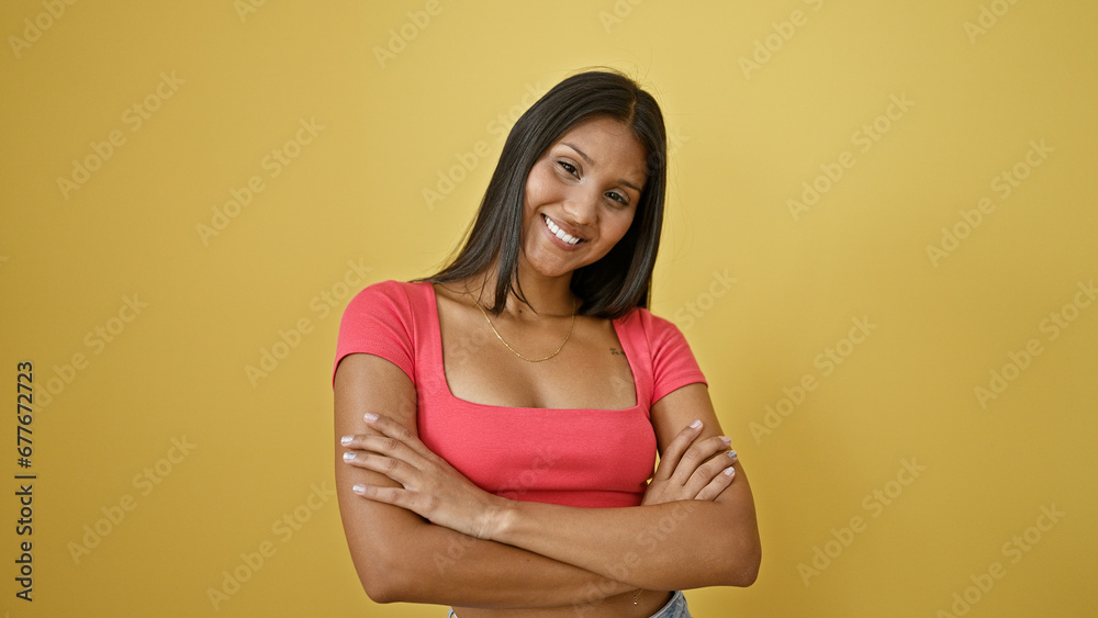 Young latin woman smiling confident standing with arms crossed gesture over isolated yellow background Young latin woman smiling confident standing with arms crossed gesture over isolated yellow background