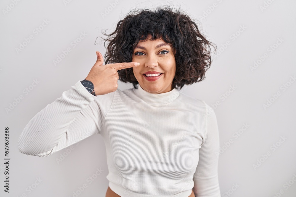 Hispanic woman with curly hair standing over isolated background pointing with hand finger to face and nose, smiling cheerful. beauty concept Hispanic woman with curly hair standing over isolated background pointing with hand finger to face and nose, smiling cheerful. beauty concept
