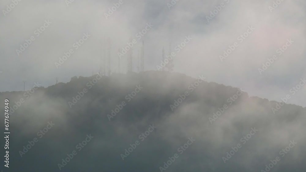 Metal turrets for receiving and transmitting satellite dishes for telecommunications and other signals on top of a mountain and partially covered by fog and low clouds.