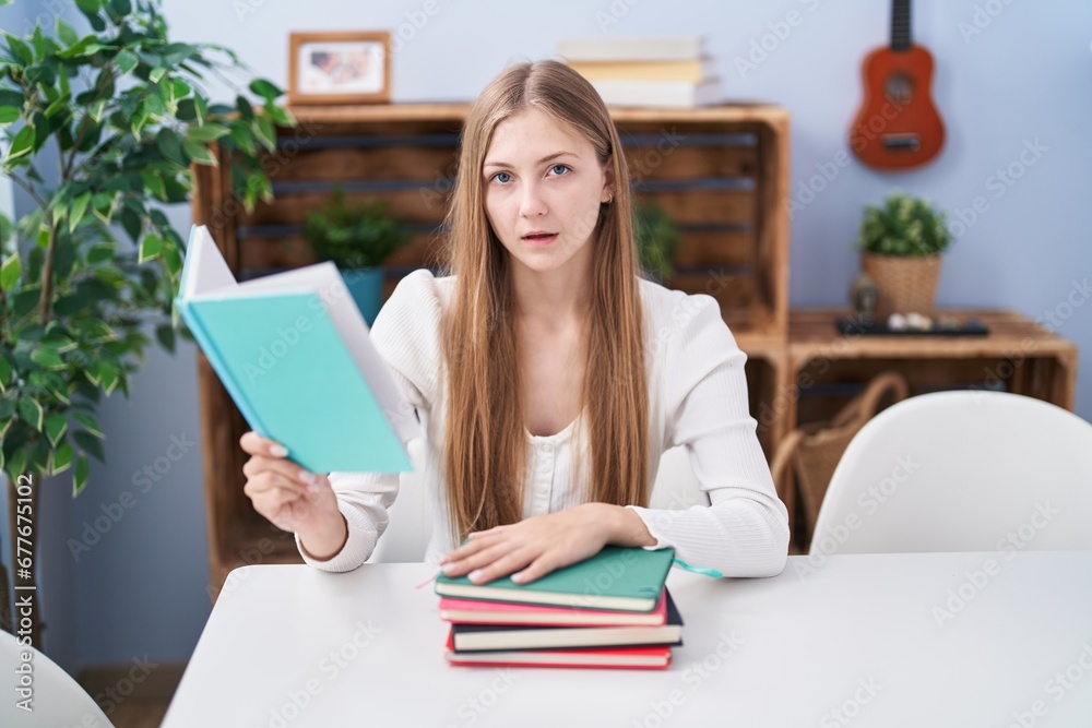 Young caucasian woman reading books at home scared and amazed with open mouth for surprise, disbelief face Young caucasian woman reading books at home scared and amazed with open mouth for surprise, disbelief face