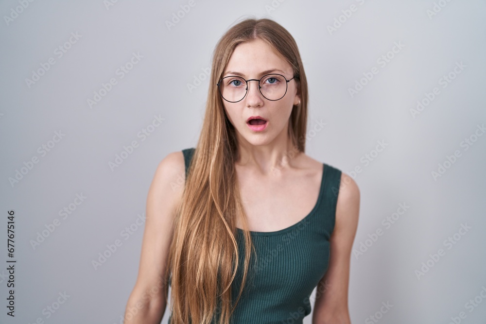 Young caucasian woman standing over white background in shock face, looking skeptical and sarcastic, surprised with open mouth