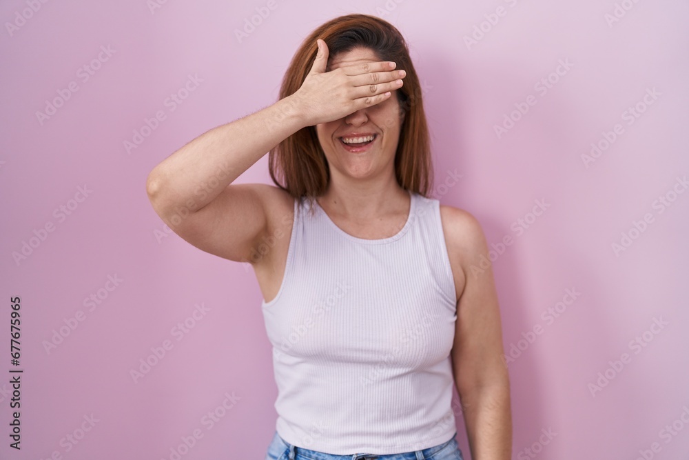 Brunette woman standing over pink background smiling and laughing with hand on face covering eyes for surprise. blind concept. Brunette woman standing over pink background smiling and laughing with hand on face covering eyes for surprise. blind concept.