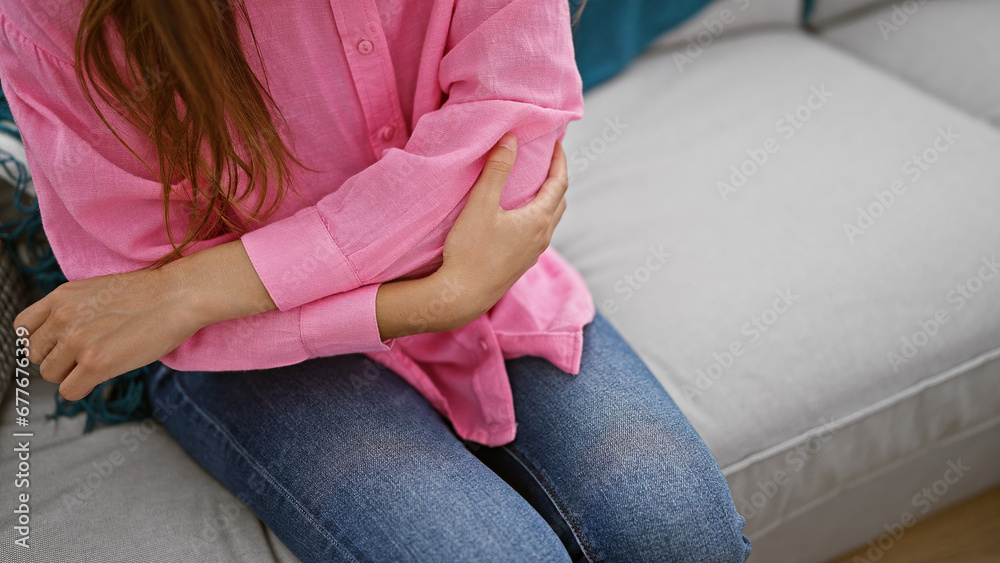Gorgeous young hispanic woman, sitting indoors on her living room sofa, sadly bearing elbow pain at her apartment home Gorgeous young hispanic woman, sitting indoors on her living room sofa, sadly bearing elbow pain at her apartment home