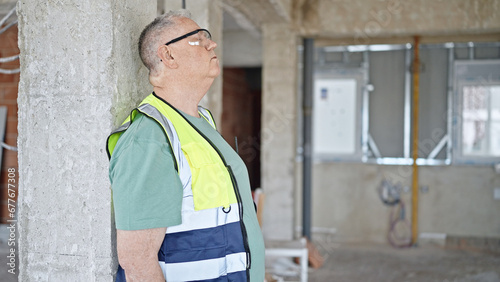 Middle age grey-haired man builder leaning on wall tired at construction site © Krakenimages.com