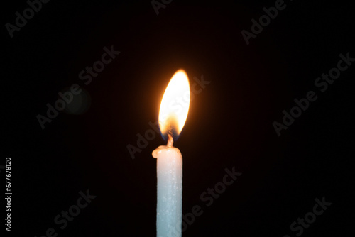 Burning candle on a black background in the dark, close-up