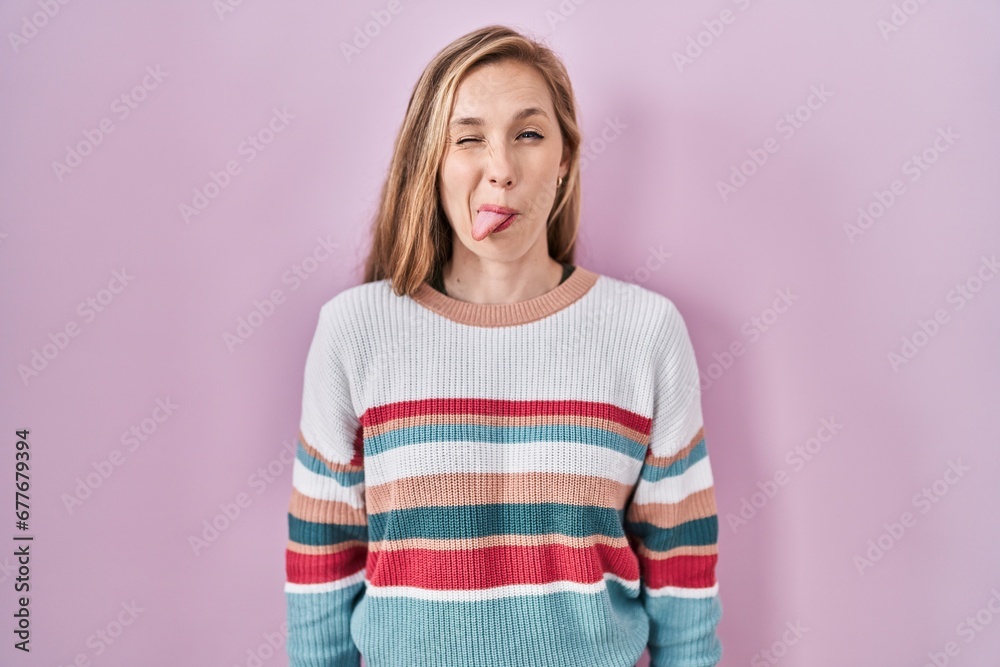 Young blonde woman standing over pink background sticking tongue out happy with funny expression. emotion concept. Young blonde woman standing over pink background sticking tongue out happy with funny expression. emotion concept.