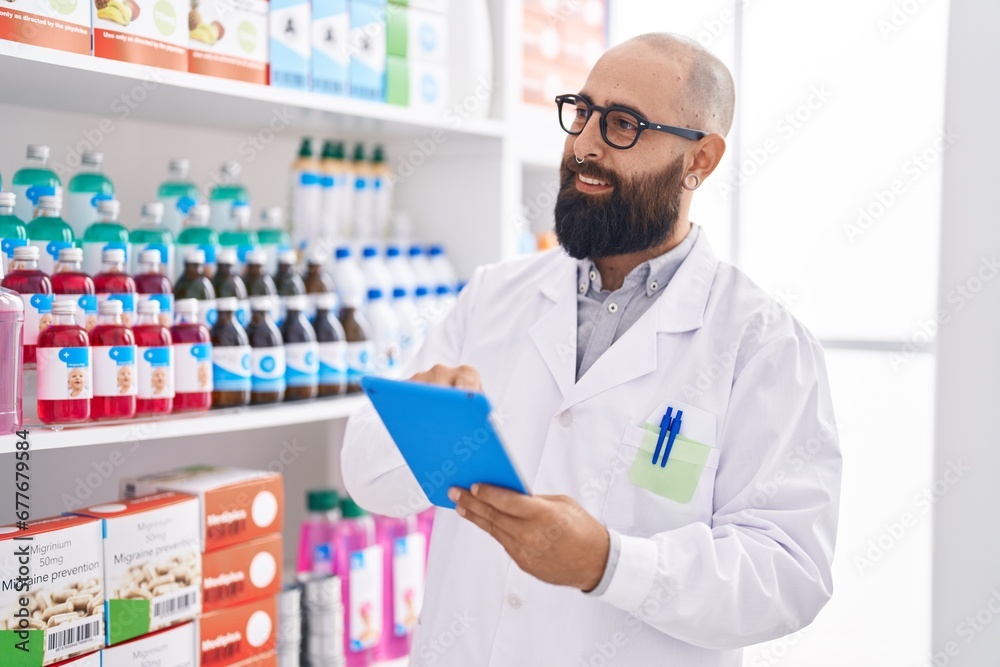 Young bald man pharmacist using touchpad working at pharmacy