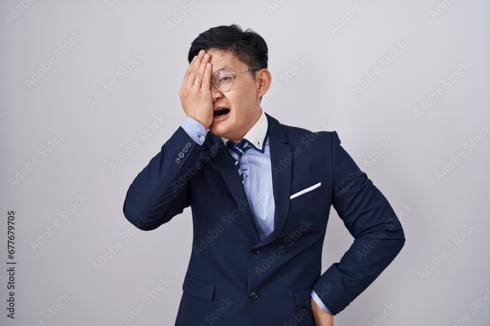 Young asian man wearing business suit and tie yawning tired covering half face, eye and mouth with hand. face hurts in pain. Young asian man wearing business suit and tie yawning tired covering half face, eye and mouth with hand. face hurts in pain.