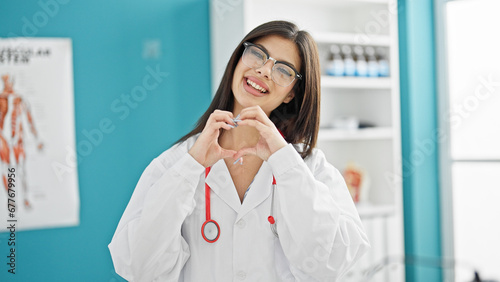 Young caucasian woman doctor smiling doing heart gesture with hands at clinic