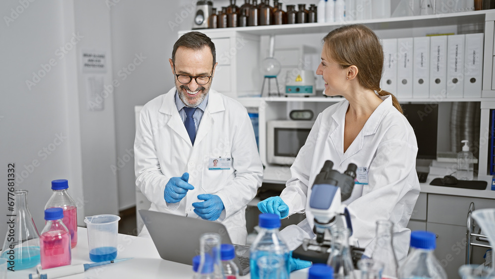 Inside the lab, two enthusiastic scientists in conversation, juggling their laptop and test tubes in an indoor laboratory