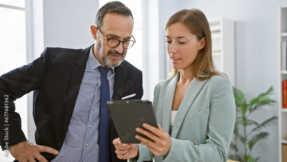 Two business workers standing together in office, engrossed in work on touchpad, epitomizing professionalism with a blend of elegant, relaxed concentration. Two business workers standing together in office, engrossed in work on touchpad, epitomizing professionalism with a blend of elegant, relaxed concentration.