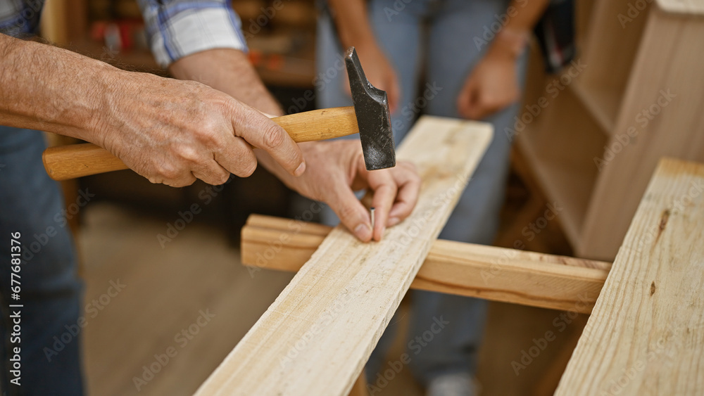 Two skilled carpenters, a dynamic duo, driving a nail into a wood plank at a lively carpentry workshop. joiner and handyman together hammering, shaping the timber into bespoke furniture Two skilled carpenters, a dynamic duo, driving a nail into a wood plank at a lively carpentry workshop. joiner and handyman together hammering, shaping the timber into bespoke furniture
