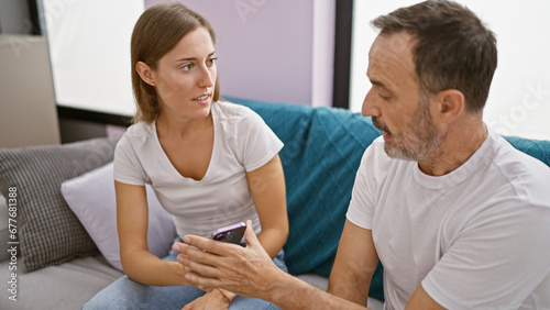 At home, father and daughter in a heated argument over smartphone usage, sitting unhappily on the sofa in their living room, expressing their disagreement in a casual, yet tense conversation.