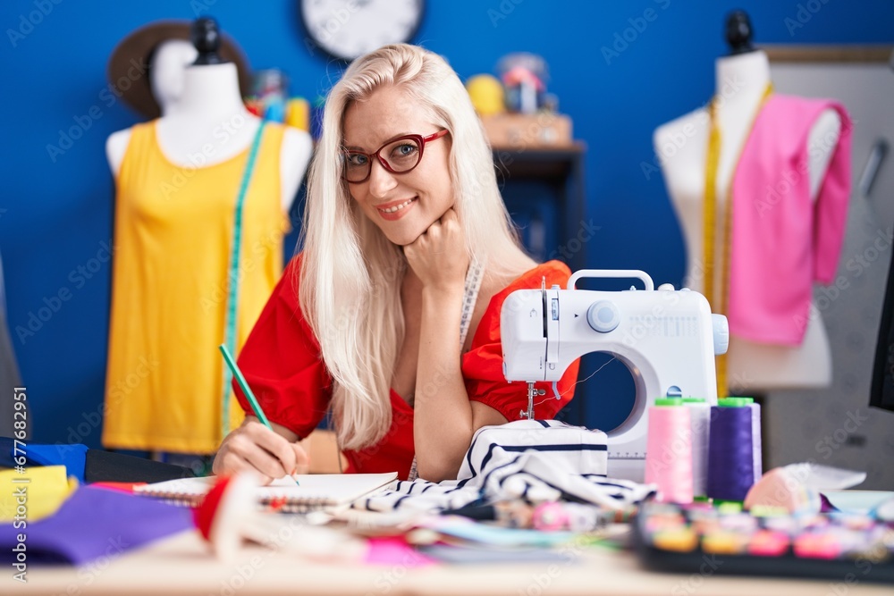 Fototapeta premium Young blonde woman tailor smiling confident drawing on notebook at sewing studio