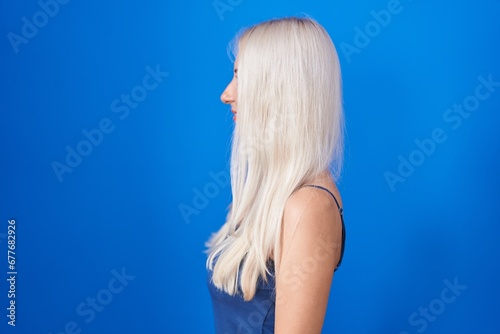 Caucasian woman standing over blue background looking to side, relax profile pose with natural face and confident smile.