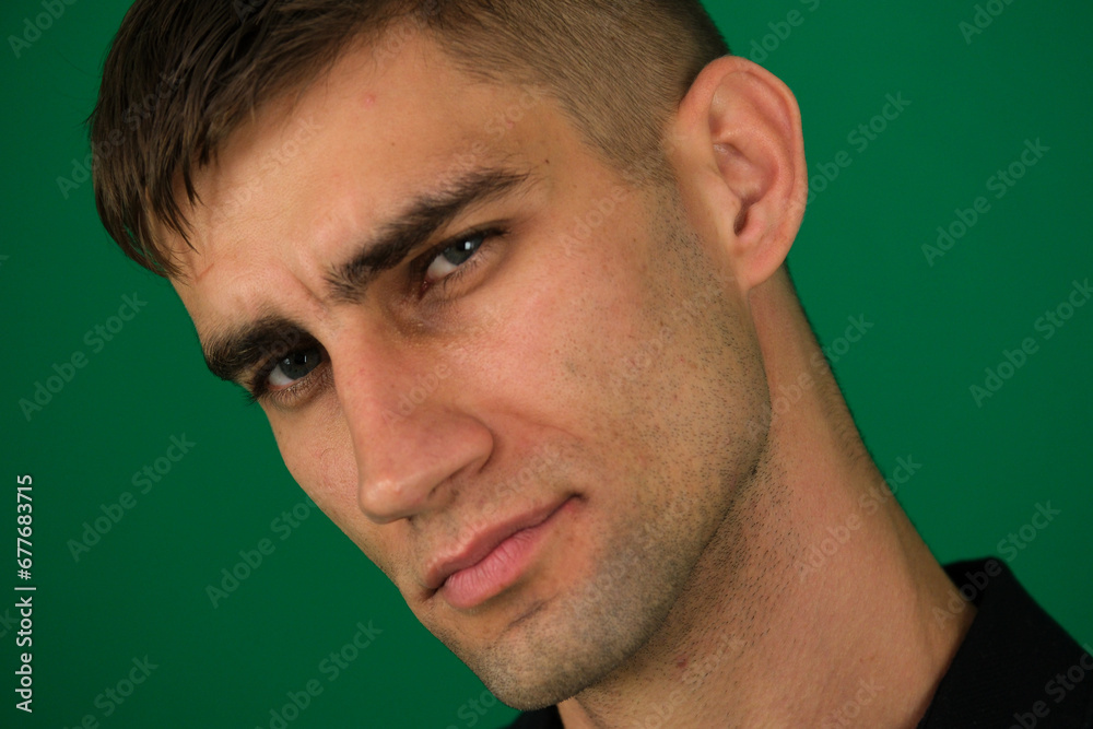 Fototapeta premium emotions of a handsome man guy on a green background chromakey close-up dark hair young man. Headshot of thoughtful handsome man, looking intrigued and squinting, thinking about something,