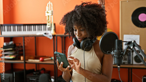 African american woman musician wearing headphones using smartphone at music studio