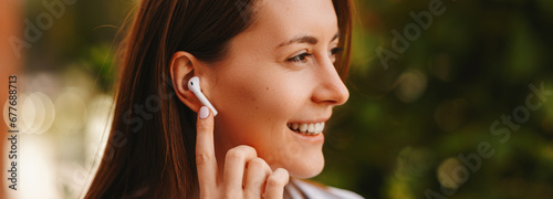 Banner photo of young joyful woman using earpods outdoor, wireless headphones. photo