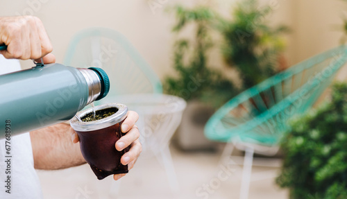A man pours water from a thermos into a mate. Yerba Mate, traditional South American hot drink.Middle age latin american man enjoying outdoors. photo
