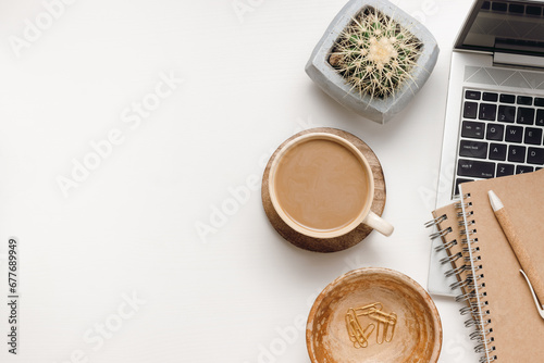 Office desk table with copy space. Workspace with laptop, coffee, notepad, office supplies and cactus in pot on white wooden table. Home office, aesthetic style, top view. photo