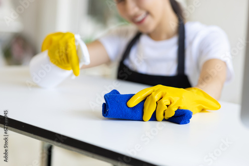 A young woman wearing an apron is cleaning a table in her home office using disinfectant and a wipe. photo