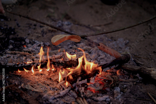 roasting bread and sausage over the burning flame of campfire. Camping concept