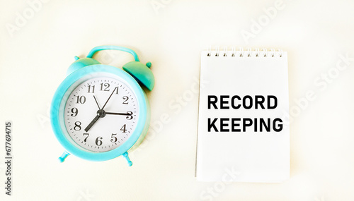 Writing the text RECORD KEEPING in a notepad with a clock on a white background