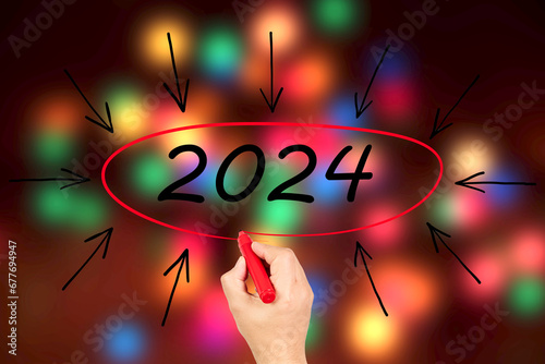 2024, Woman writing the number 2024 on background of faded lights. Happy New Year