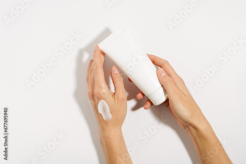 female hands with a smear of cream on the skin hold a white tube mockup on a white isolated background. the concept of moisturizing and nourishing the skin, beauty products and cosmetology.