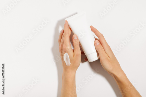 Female hands with a smear of moisturizer holding a white mockup tube of face or body cream on a white isolated background. Concept of skin care, beauty products. Image for your design