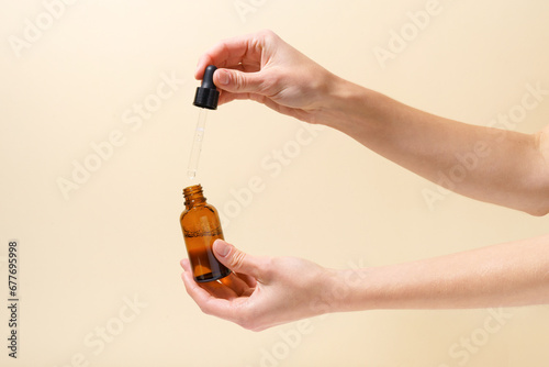 Close-up of female hands holding serum and pipette dispenser on beige isolated background. The concept of nourishing and moisturizing the skin of the face, reducing wrinkles and signs of aging
