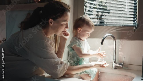Young Mother and Little Baby Child Playing with Water Flowing from a Tap