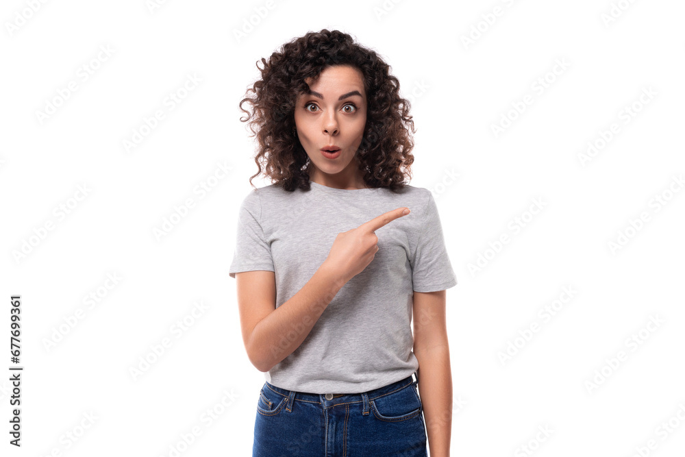 surprised european woman with black curly hair in a gray basic t-shirt points her fingers towards advertising space surprised european woman with black curly hair in a gray basic t-shirt points her fingers towards advertising space