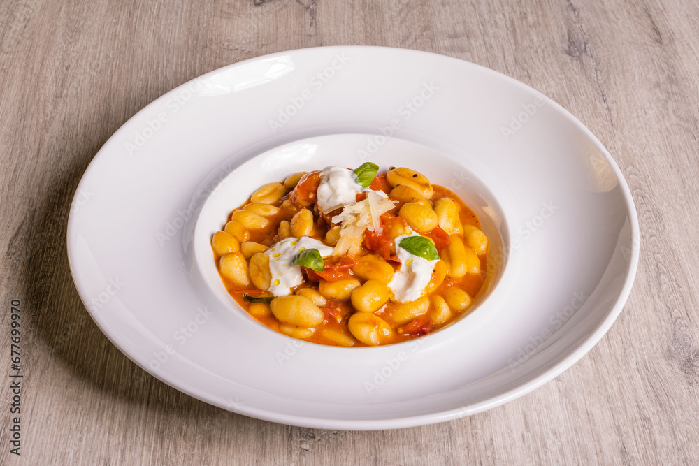 Piatto di gnocchi con pomodori, burrata pugliese, basilico e formaggio grattugiato servito come primo piatto in un ristorante Piatto di gnocchi con pomodori, burrata pugliese, basilico e formaggio grattugiato servito come primo piatto in un ristorante