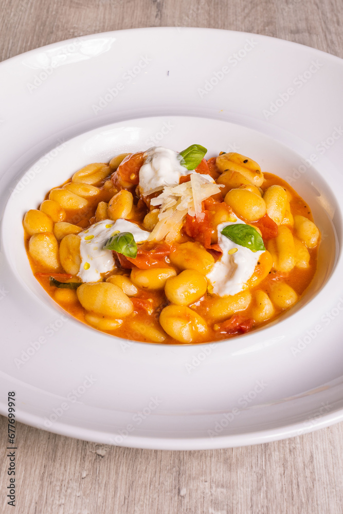 Piatto di gnocchi con pomodori, burrata pugliese, basilico e formaggio grattugiato servito come primo piatto in un ristorante