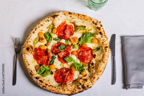 Pizza tradizionale napoletana con salame piccante, mozzarella, basilico e pomodorini gialli servita in una pizzeria photo